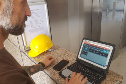 Tecnico UtopiX esamina software timelapse su tablet Panasonic in cantiere con elmetto Tecnico con barba esamina il software UtopiX timelapse su tablet Panasonic con elmetto giallo sul tavolo e certificato