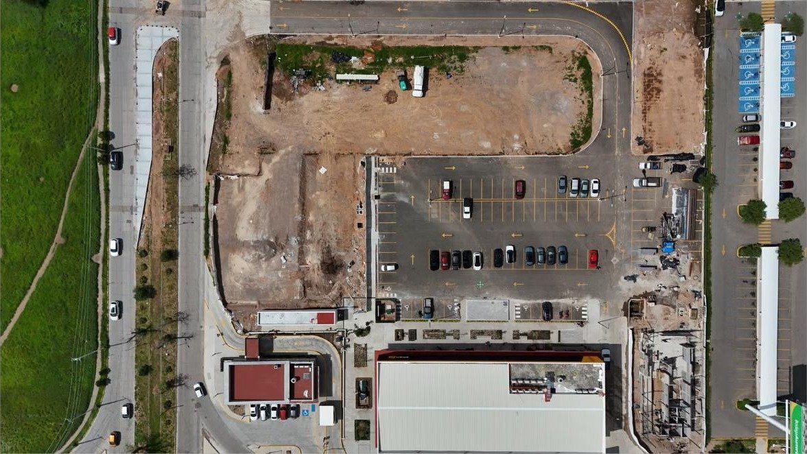 Vista zenitale di un'area di cantiere affiancata alla viabilità esistente Vista dall'alto di un'area di cantiere accanto a una strada, con parcheggi, edifici e aree di scavo